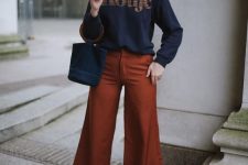 24 a simple and contrasting outfit with a navy printed sweatshirt, rust-colored flare trousers, brown boots and a navy bucket bag