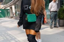 Ariana Grande wearing an oversized black hoodie as a mini dress, a green waist bag and black over the knee boots