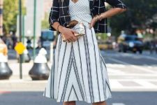 With checked V-neck top, black and white striped A-line knee-length skirt, golden clutch and white ankle strap high heels