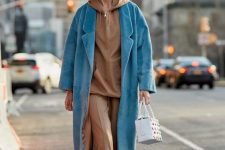 a beige oversized hoodie paired with matching cropped pants, white mules, a blue coat and a white bag for a trendy look