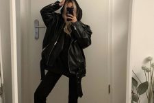 a black hoodie, flare trousers, white sneakers and an oversized black leather jacket