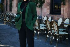 a black turtleneck, black cropped trousers, boots, a green blazer and a green mini bag for working