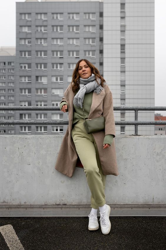 a lovely fall outfit with a green sweatshirt, sweatpants, white sneakers, a beige coat, a grey scarf and a green bag for every day