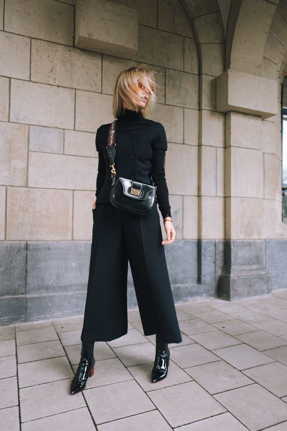 a refined outfit with a black turtleneck and a waistcoat with buttons, culottes, lacquer boots and a matching bag