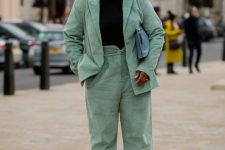 a stylish work outfit with a pale green pantsuit, a black turtleneck, two color boots and a light blue bag