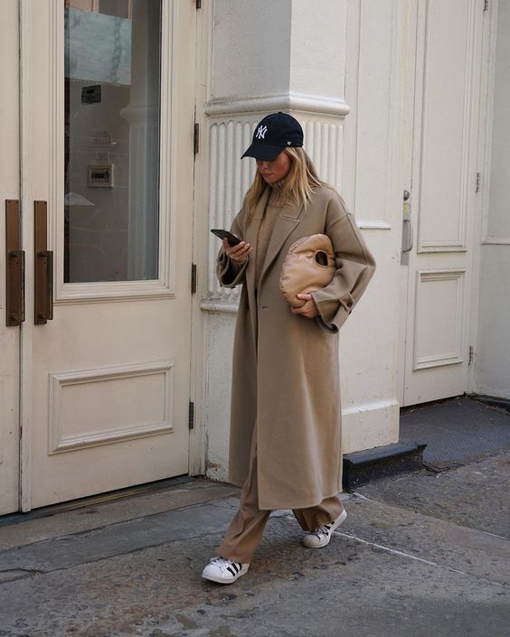 a total beige look with a turtleneck, trousers, a midi coat, white sneakers and a cap plus a beige bag