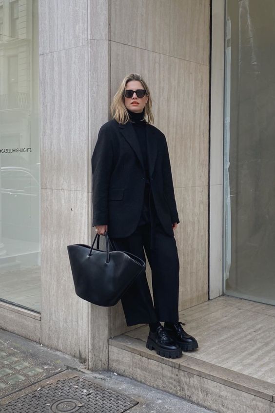 a total black look with a turtleneck, wide leg trousers, platform shoes, an oversized blazer and a tote for work or for every day