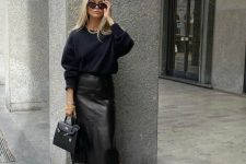 a total black work look with a sweatshirt, a plain leather midi skirt, chunky boots and a bag