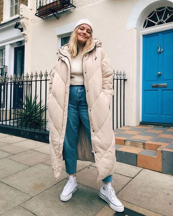 a pretty winter look with a neutral top, light blue jeans, white sneakers, a tan midi puffer coat and a white beanie
