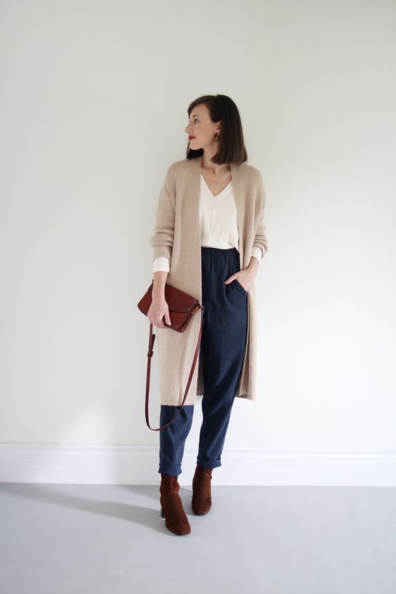 a stylish casual look with a white top, navy trousers, burgundy boots and a bag, a tan long cardigan