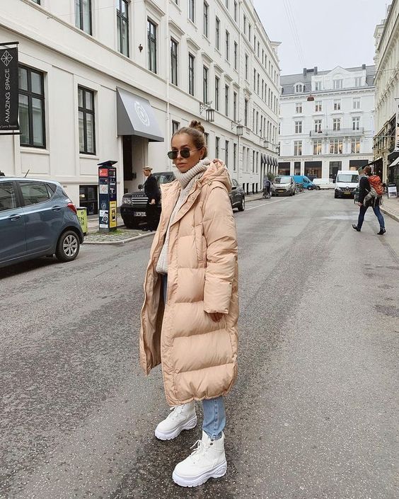 a neutral winter outfit with an off-white sweater, light blue jeans, a tan puffer coat, white boots is chic