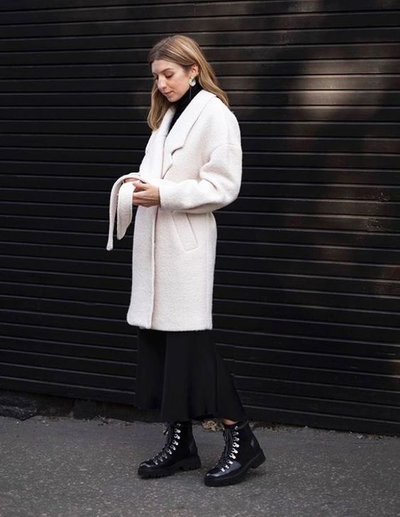 an elegant winter outfit with a black turtleneck, a black midi skirt, black hiking boots and a white faux fur coat