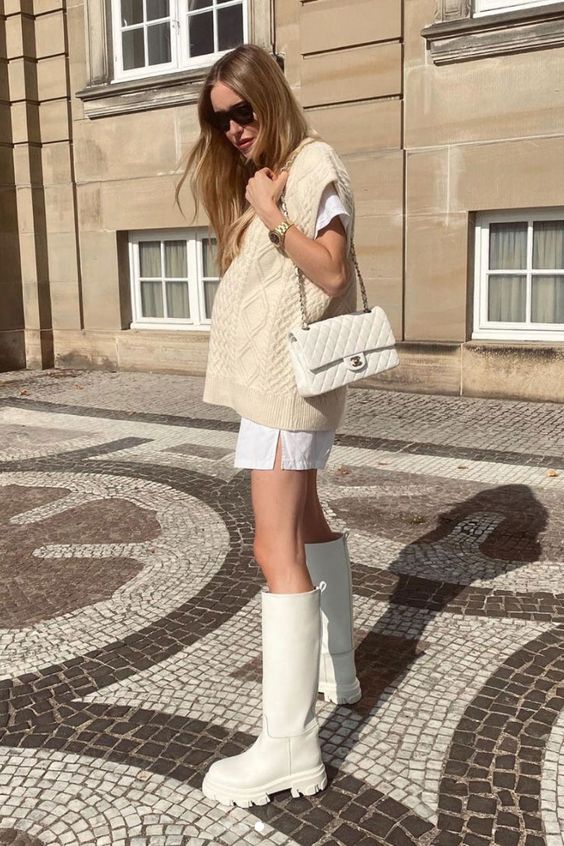 an all-neutral outfit with a white t-shirt mini dress, a creamy patterned chunky vest, a creamy bag and white kneed platform boots