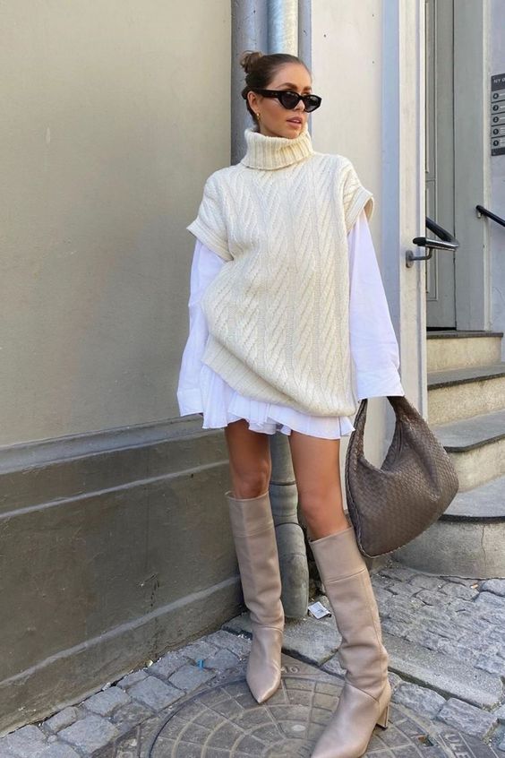 a chic winter outfit with a white mini shirtdress, a creamy chunky knit vest, tan knee boots and a taupe bag