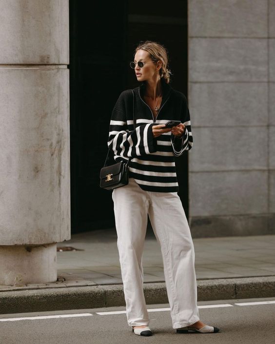 a black and white striped zip sweater, white jeans, two-tone shoes and a small black bag