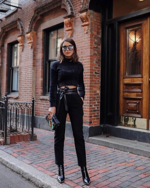 With black cropped pants, black leather belt, mirrored sunglasses, colorful clutch and black embellished boots