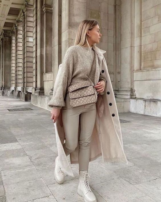 a neutral winter outfit with a tan sweater, tan leather leggings, white chunky boots, a coat and a bag