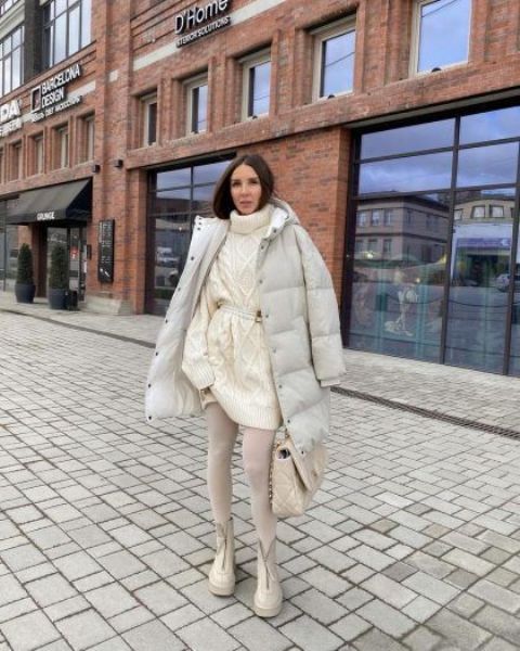 a total neutral outfit with a white patterned sweater dress, white tights, white chunky boots, a puff jacket and a creamy bag