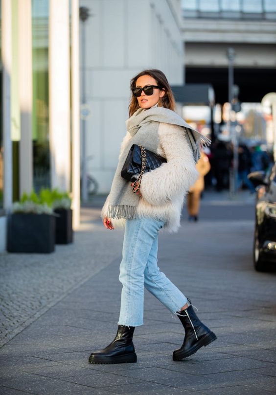 a white faux fur jacket, light blue jeans, black chunky boots, a black bag and a grey scarf