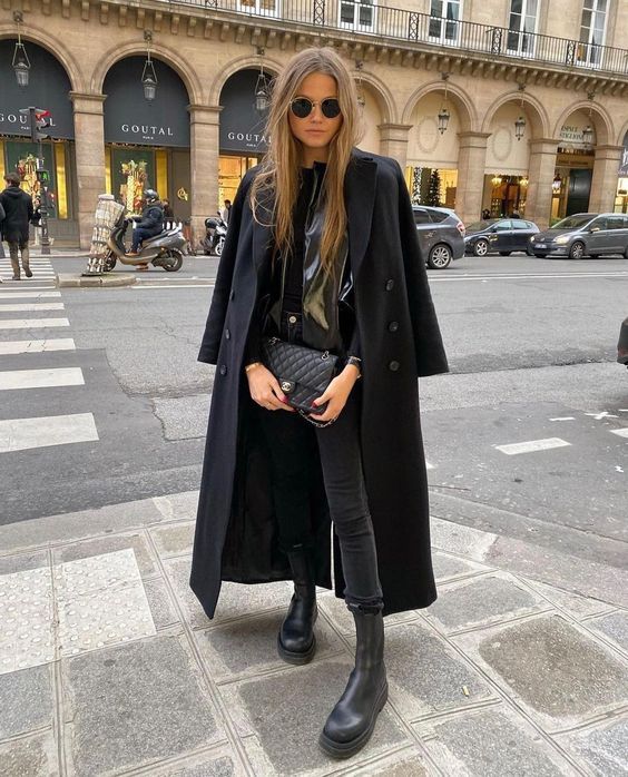 an all black winter outfit wiht a leather blazer, jeans, chunky Chelsea boots, a coat and a bag