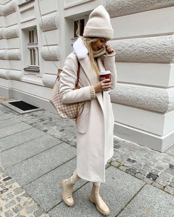 an all neutral winter outfit with a coat, jeans, Chelsea boots, a beanie and a printed bag