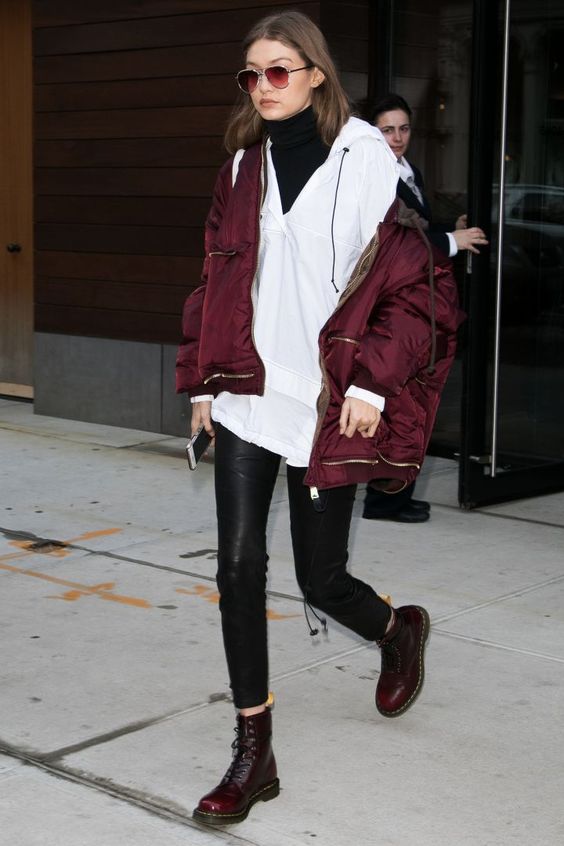 Gigi Hadid wearing a black turtleneck, a white hoodie, black leather leggings, burgundy boots and a puffer jacket