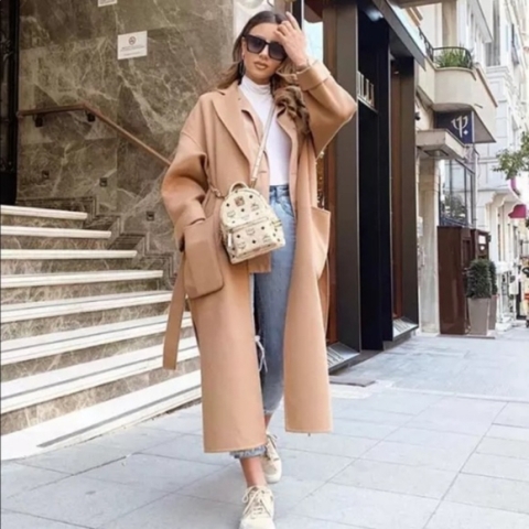With white turtleneck, cropped jeans, light brown midi coat, printed backpack, sunglasses and beige sneakers