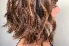 a beautiful and chic dark brown long bob with messy waves and delicate caramel balayage that gives much dimension to the hair