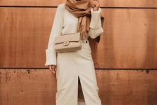 a beautiful neutral winter work look with a white chunky swater, a white midi skirt with a slit, tall white boots, a grey bag and a brown scarf
