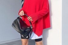 a bold look with leather biker shorts, an oversized white shirt, a colorful asymmetrical red sweater, red knee boots and a black bag