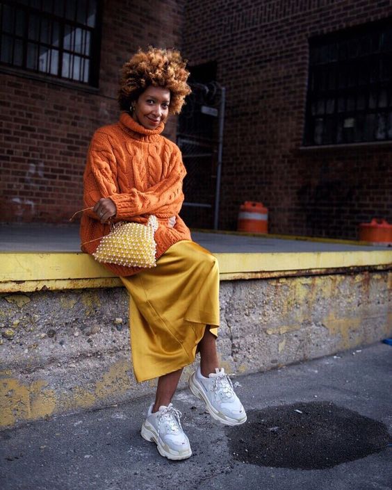 a bright outfit with an oversized orange braided sweater, a mellow yellow slip skirt, white trainers and an embellished bag