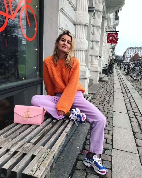 a colorful look with an orange braided sweater, lilac trousers, blue trainers and a pink bag is wow