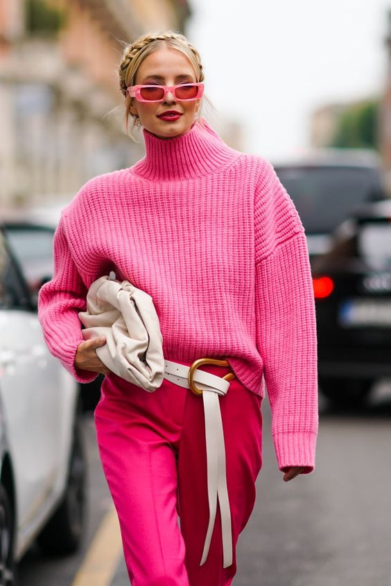 a hot pink chunky knit turtleneck sweater, red trousers, a white bag and belt, pink singlasses