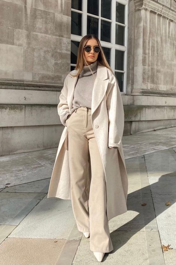a minimalist neutral winter outfit with a grey turtleneck sweater, tan high waisted pants, white boots and a white coat