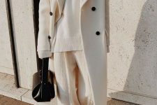 a minimalist winter look with an oversized sweater, wideleg pants, black boots, a black bag and a white coat with black buttons