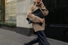 a minimalist winter work outfit with a tan oversized sweater, a black slip midi skirt, black chunky boots and a clutch