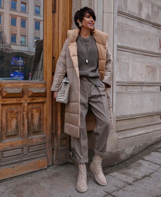 a monochromatic winter outfit with a grey sweater, grey trousers, light tan boots, a grey and tan puffer coat and a grey bag