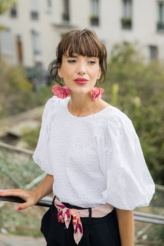 a pretty retro chic outfit with a lace blouse with puff sleeves, black trousers with a colorful sash and pink flower earrings for an accent