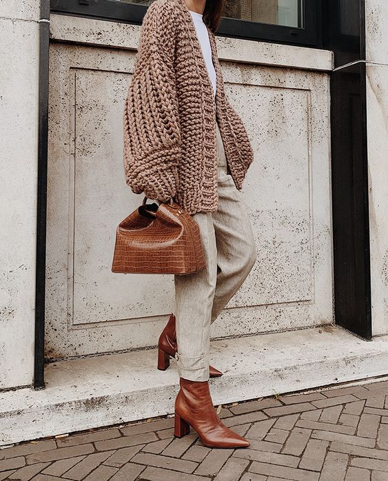 a stylish outfit with a white t shirt, light grey trousers, a beige chunky oversized cardigan, brown boots and a brown bag
