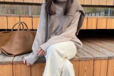 a tan oversized sweater, a greige oversized sweater on top, white jeans, black boots and a beige tote for work