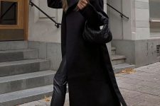a total black look with a top, leather leggings, Chelsea boots, a midi coat and a small woven bag