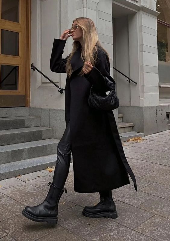 a total black look with a top, leather leggings, Chelsea boots, a midi coat and a small woven bag