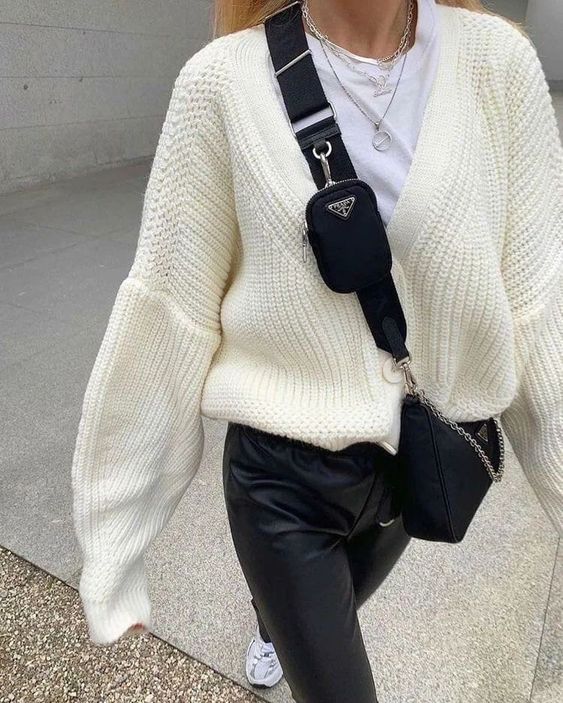 a white t-shirt, a creamy chunky cardigan, black leather trousers, a black bag and layered necklaces for a comfy outfit