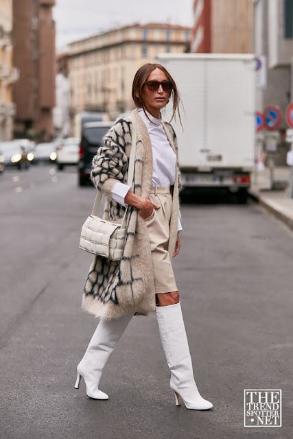 a white turtleneck, creamy leather shorts, white knee boots, a fuzzy oversized printed cardigan and a white bag