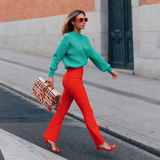 an emeral sweater, red fitting trousers, red heels and a printed bag plus a red framed sunglasses