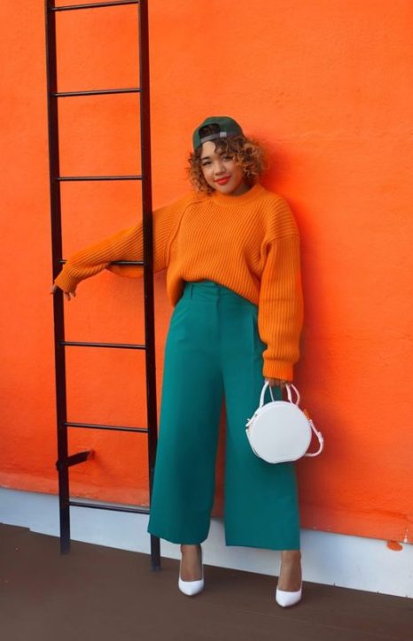 an orange chunky knit sweater, teal wideleg trousers, white shoes and a white round bag