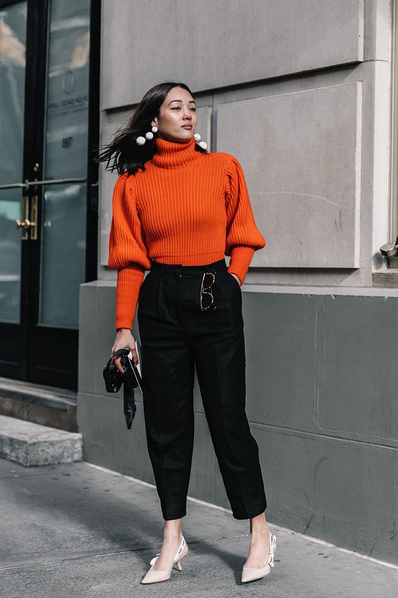 an orange sweater with puff sleeves, black trousers, nude heels, a black bag and statement white earrings