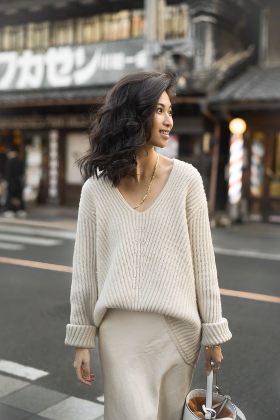 an oversized chunky creamy sweater with a V-neckline, a neutral slip skirt and a bucket bag for a feminine work look