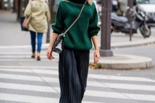 an oversized green turtleneck sweater, a black pleated midi, black boots, a black bag on chain for a chic holiday work look