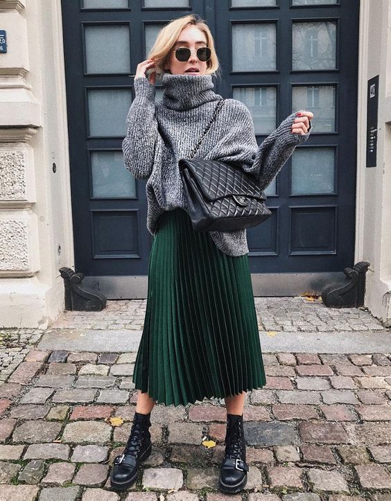 an oversized grey turtleneck sweater, a green pleated midi skirt, black combat boots and a large black bag